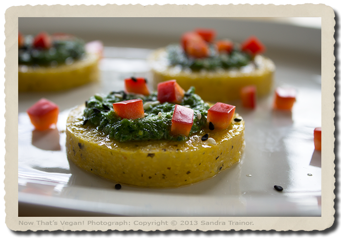 An appetizer made with precooked polenta, pesto sauce, and red bell pepper.